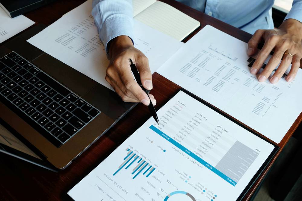 5 Retirement Mistakes Small-Business Owners Make (And How to Avoid Them) 3 Hands with a pen reviewing printed financial reports beside a laptop