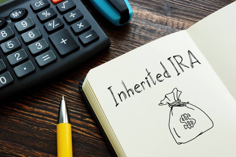 A Guide to Individual Retirement Accounts (IRAs) 3 Notebook page reading “Inherited IRA” with a drawn money bag, beside a calculator and pen