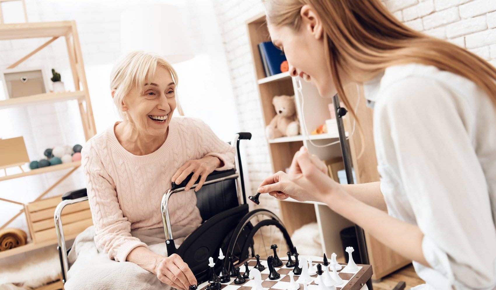 Older woman using a wheelchair playing chess with a caregiver at home – long-term care planning