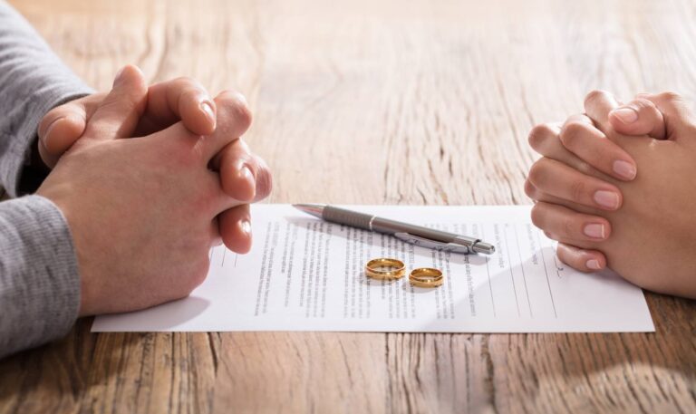 Two people's clasped hands across a table with a signed divorce agreement and wedding rings – financial planning after divorce