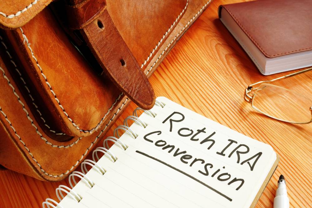 A Guide to Individual Retirement Accounts (IRAs) 7 Notebook reading “Roth IRA Conversion” beside a leather bag and reading glasses